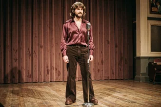 Chanteur britannique des années 70 sur scène avec chemise à col pelle à tarte et pantalon patte d'éléphant dans une salle de concert vintage